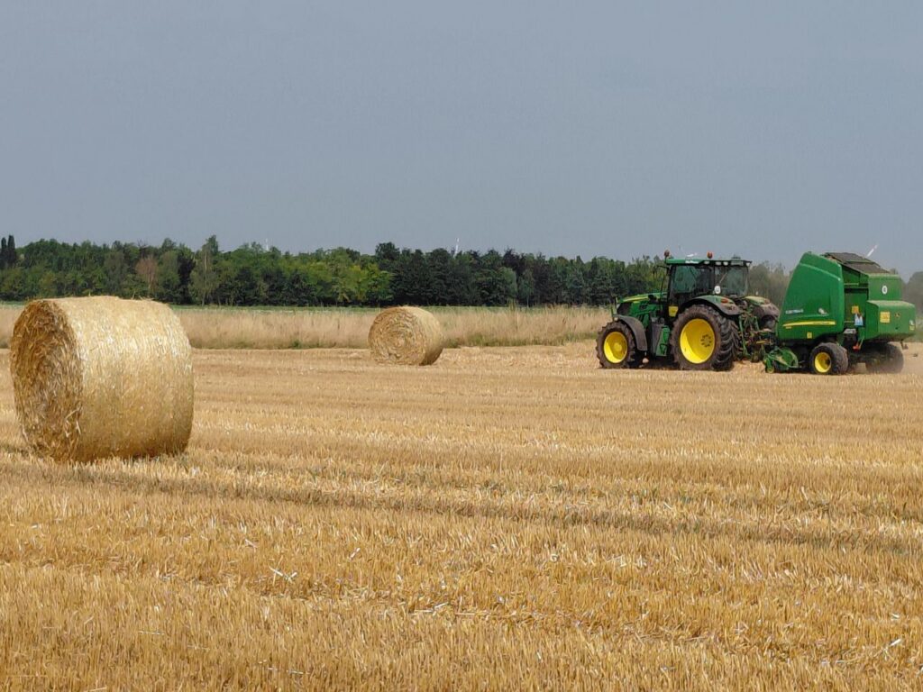 A green tractor baling straw outdoors in a field near Neuss, Germany.